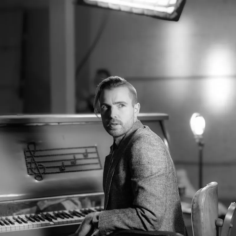 Jesse Nolan at an upright piano decorated with musical notes, looking over his shoulder, for Caught a Ghost’s “Get Your Life”