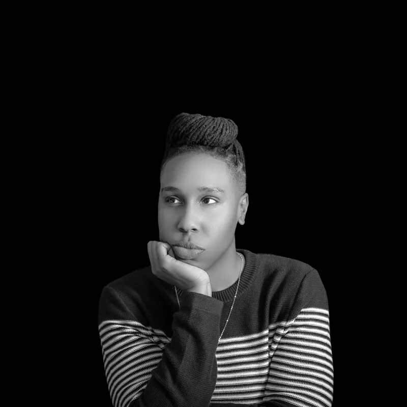 Lena Waithe in a striped sweater, chin resting on her hand, against a black background