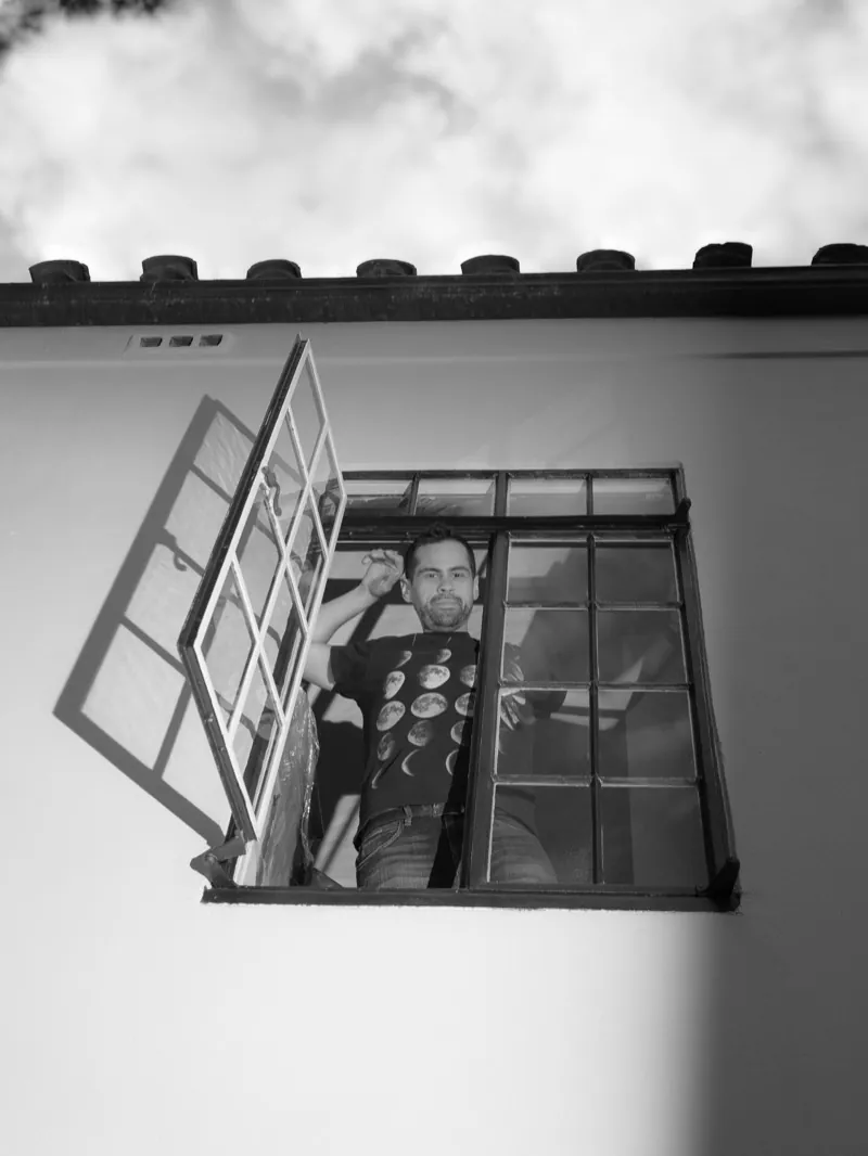 Man leaning out of an open window high on a white wall, seen from below