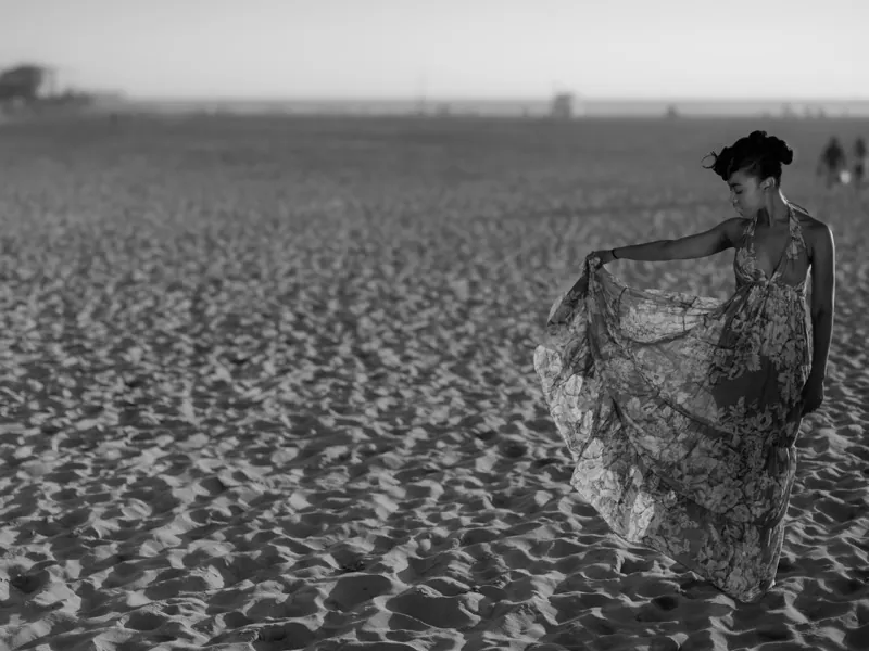 Nia Jervier on a sandy beach, holding out the skirt of a floral maxi dress