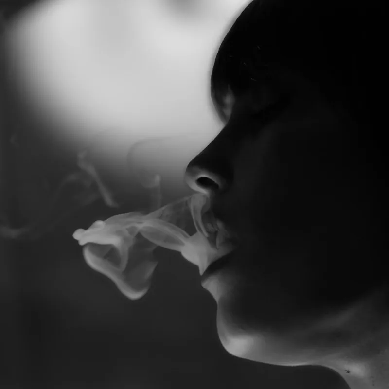 Close-up profile of a person exhaling a curl of smoke against a dark background