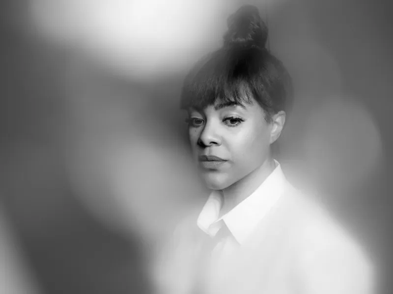 Woman with bangs and a top knot in a white collared shirt, framed by soft blurred light