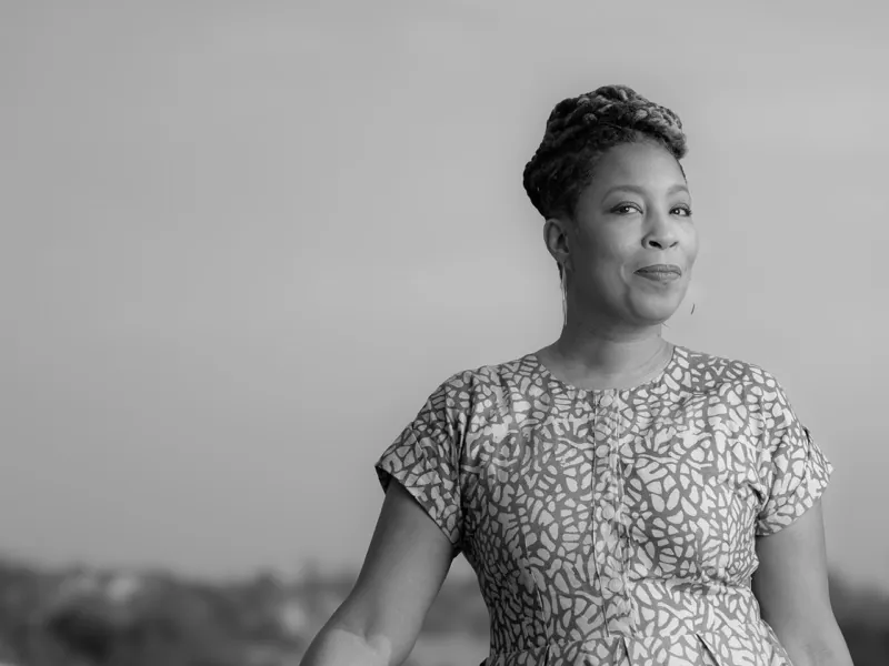 Smiling woman with braided hair in a patterned dress, photographed outdoors against the sky