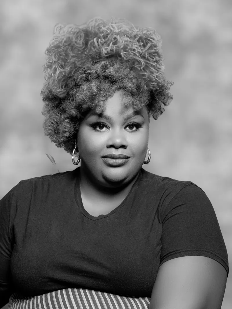 Woman with a tall curly updo and hoop earrings, looking at the camera