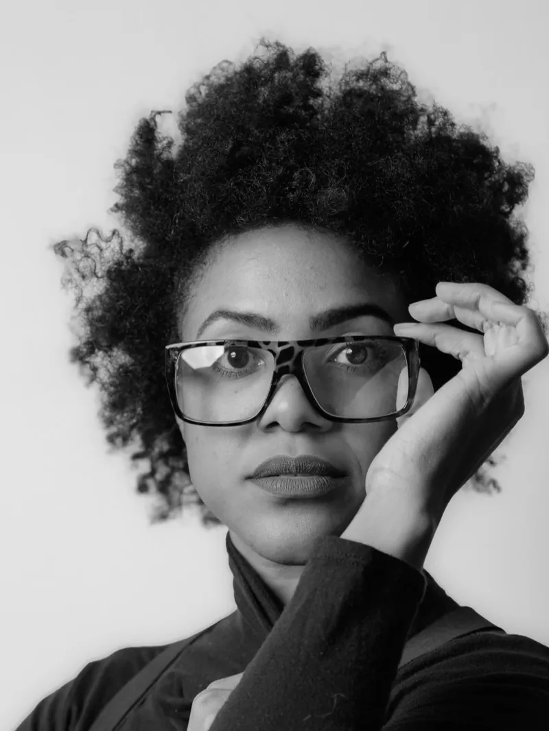 Woman with natural curly hair adjusting large tortoiseshell glasses