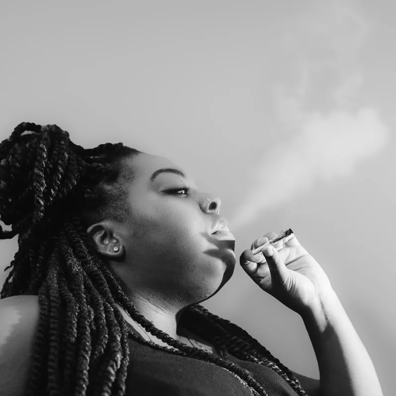 Woman with twisted braids gathered up, exhaling a stream of smoke