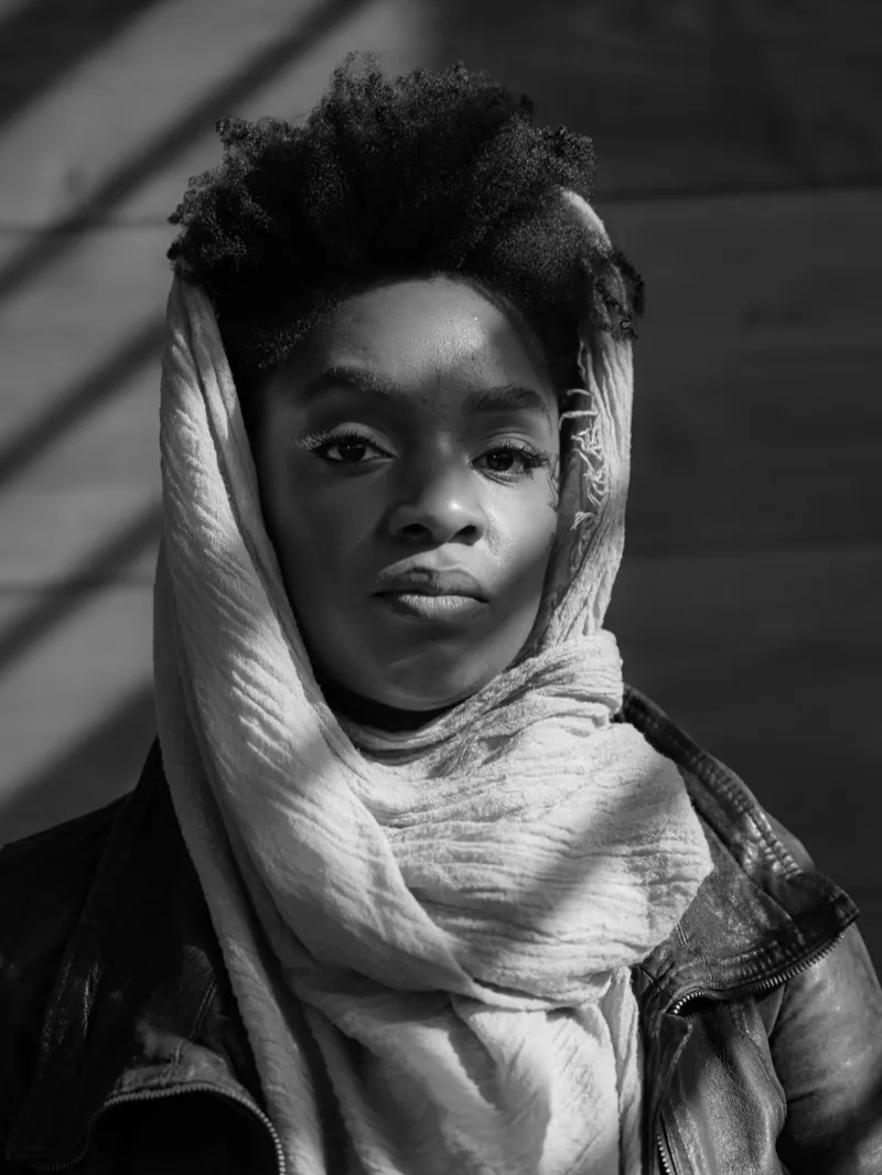 Woman with short natural hair, a pale scarf draped over her head, in a leather jacket