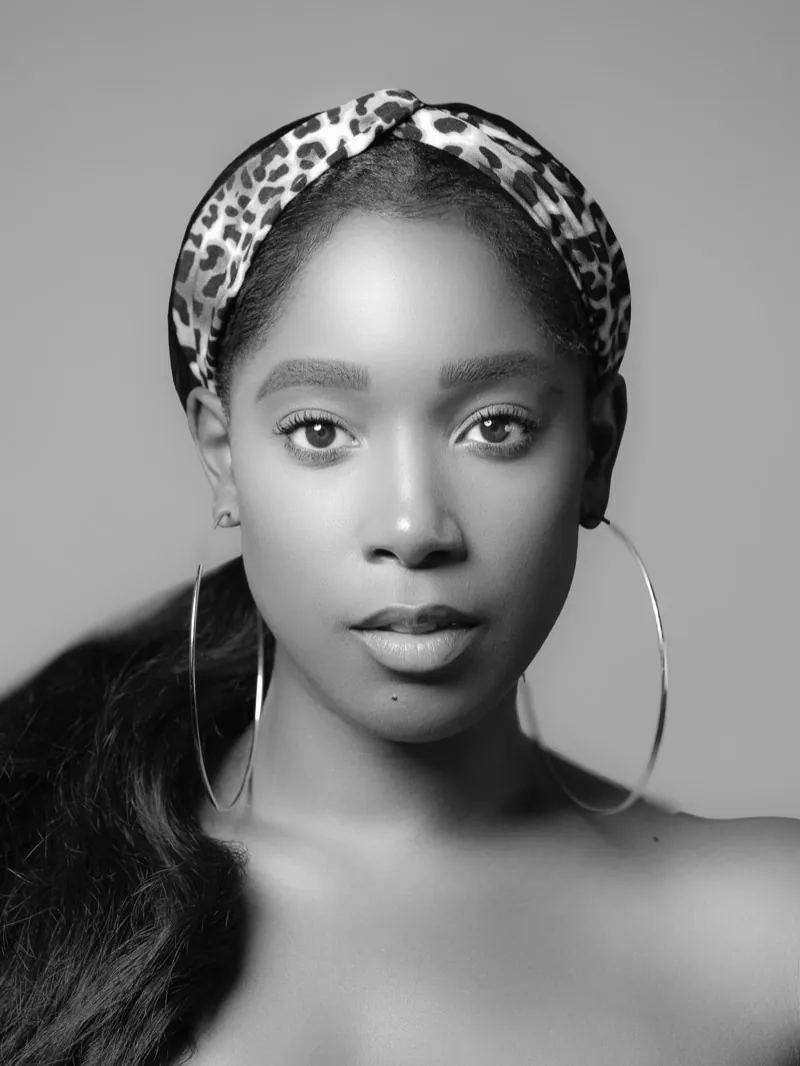 Woman in a leopard-print headband and large hoop earrings against a gray backdrop